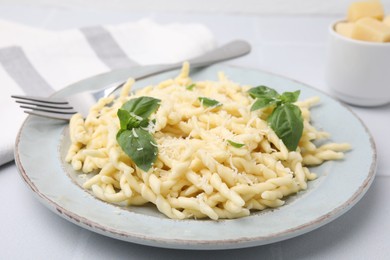 Plate of delicious trofie pasta with cheese and basil leaves on white tiled table