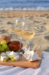 Photo of Glasses with white wine and snacks for beach picnic on sandy seashore