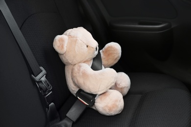 Photo of Child's toy bear buckled with safety belt on car backseat. Prevention of danger