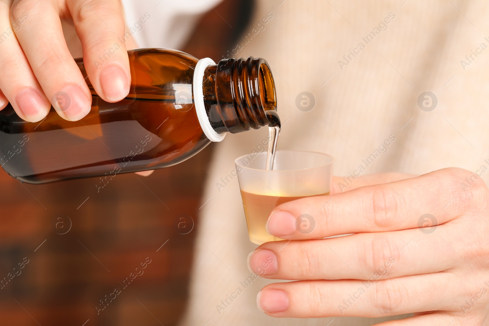 Photo of Woman pouring syrup from bottle into measuring cup, closeup. Cold medicine