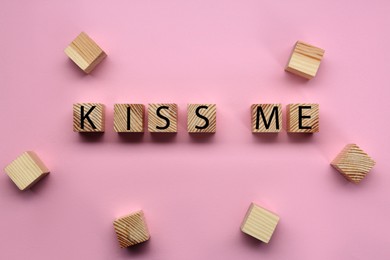 Wooden cubes with phrase Kiss Me on pink background, flat lay