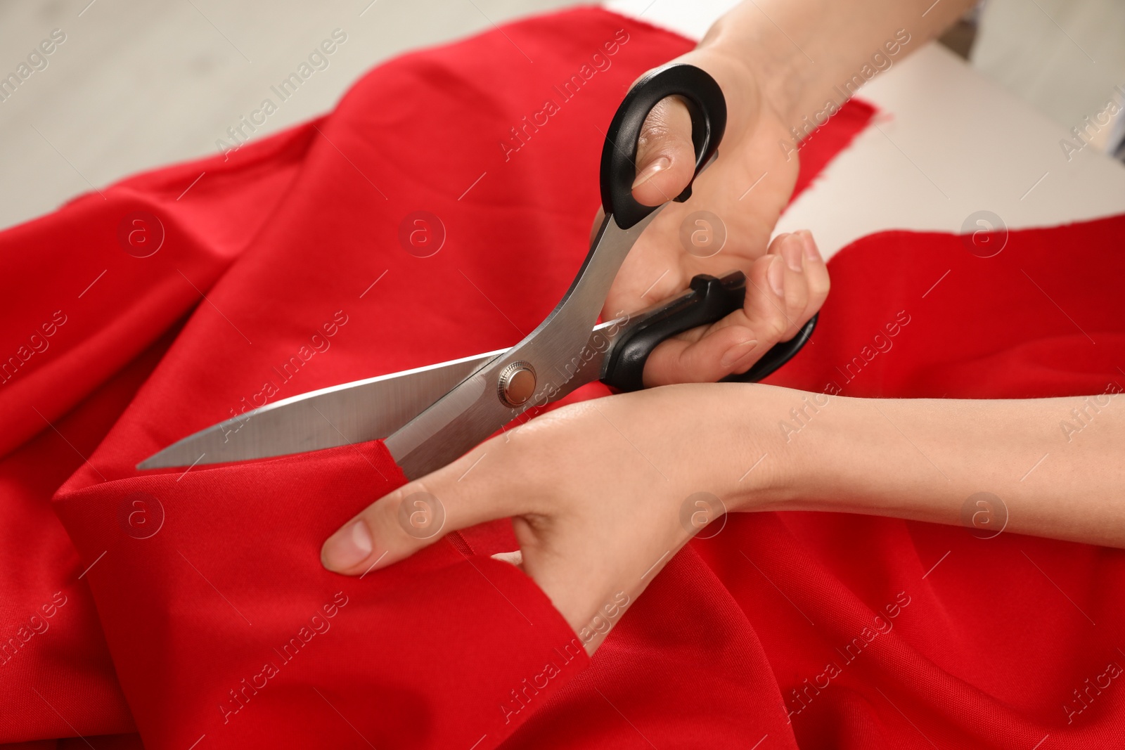 Photo of Woman cutting fabric with sharp scissors at white table, closeup