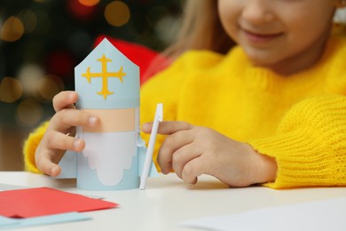 Cute little girl with paper Saint Nicholas toy at home, closeup
