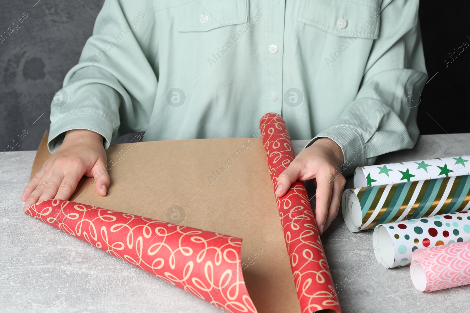 Photo of Woman with roll of beautiful wrapping paper at light grey table, closeup