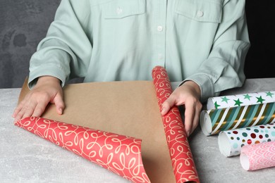 Photo of Woman with rollbeautiful wrapping paper at light grey table, closeup
