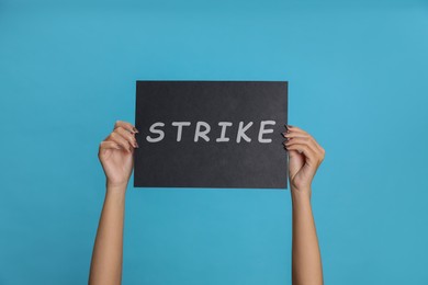 Woman holding sign with word Strike on light blue background, closeup