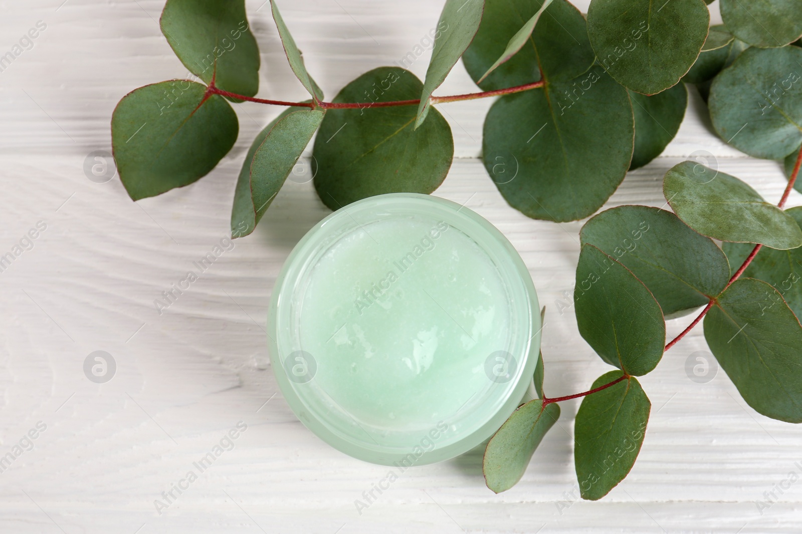 Photo of Homemade cosmetic product and eucalyptus leaves on white wooden table, flat lay