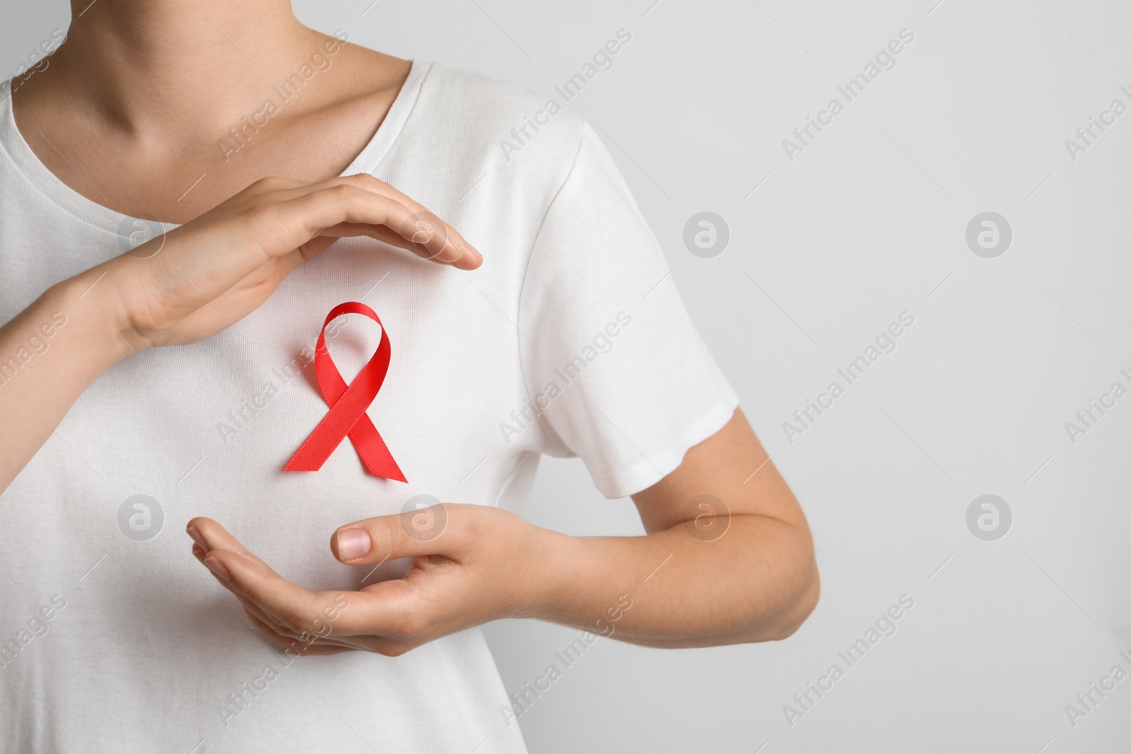 Photo of Woman with red ribbon on t-shirt against light background. Cancer awareness