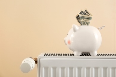 Photo of Piggy bank with money on heating radiator against light background. Space for text