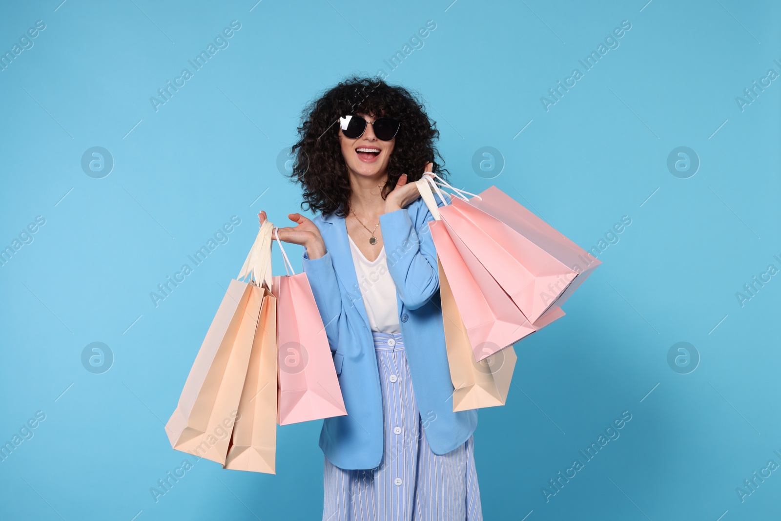 Photo of Happy young woman with shopping bags and stylish sunglasses on light blue background