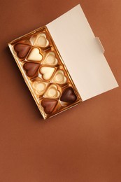 Photo of Partially empty box of chocolate candies on brown background, top view. Space for text