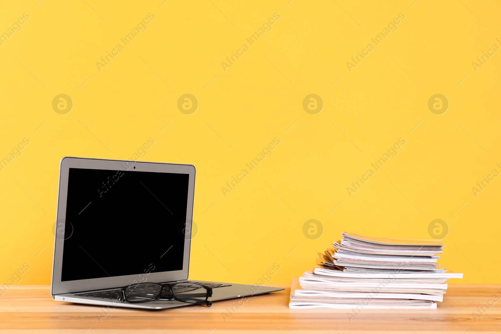 Photo of Laptop, glasses and stack of magazines on wooden table. Space for text