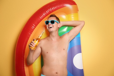 Shirtless man with inflatable mattress and bottle of drink on color background