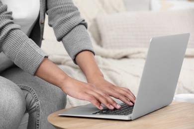 Photo of Woman using laptop at wooden coffee table indoors, closeup