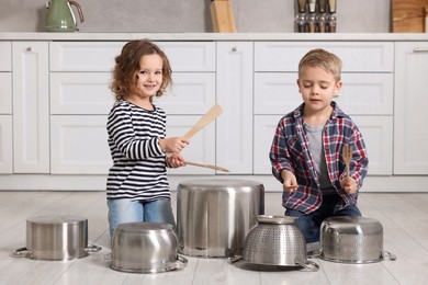 Photo of Little children pretending to play drums on pots in kitchen