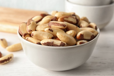 Bowl with tasty Brazil nuts on white table