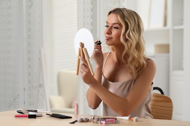 Photo of Beautiful makeup. Woman with mirror applying liquid lipstick at home