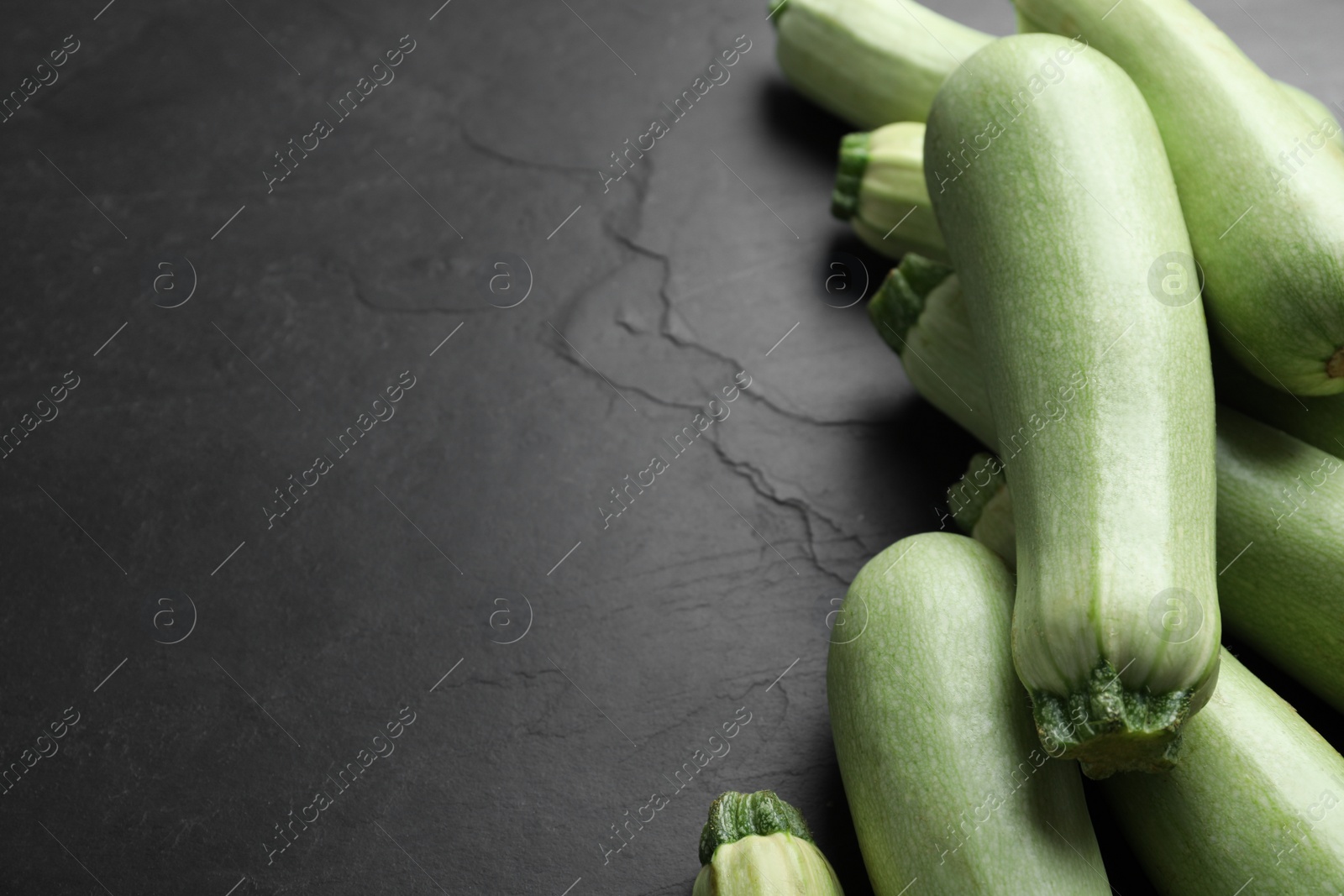 Photo of Raw green zucchinis on black slate table, closeup. Space for text