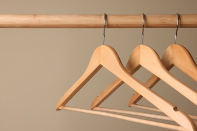 Photo of Clothes hangers on wooden rail against beige background, closeup