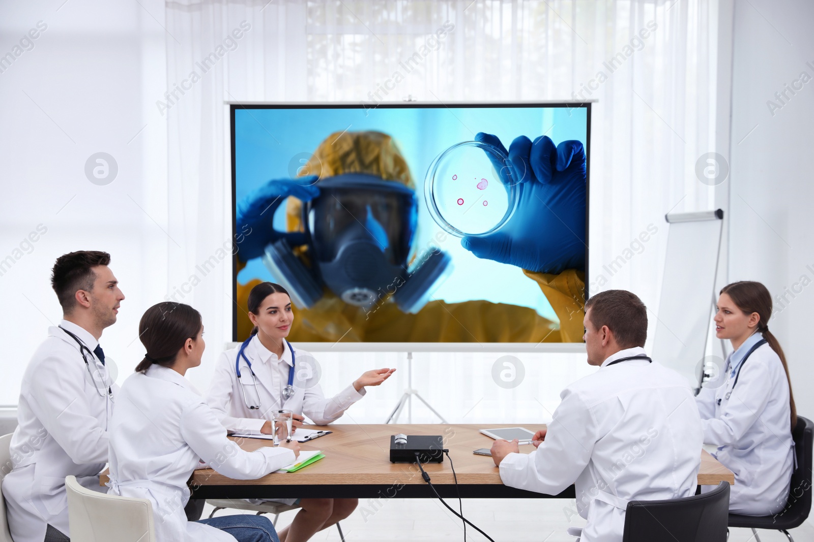 Image of Team of doctors using video projector during coronavirus conference in office