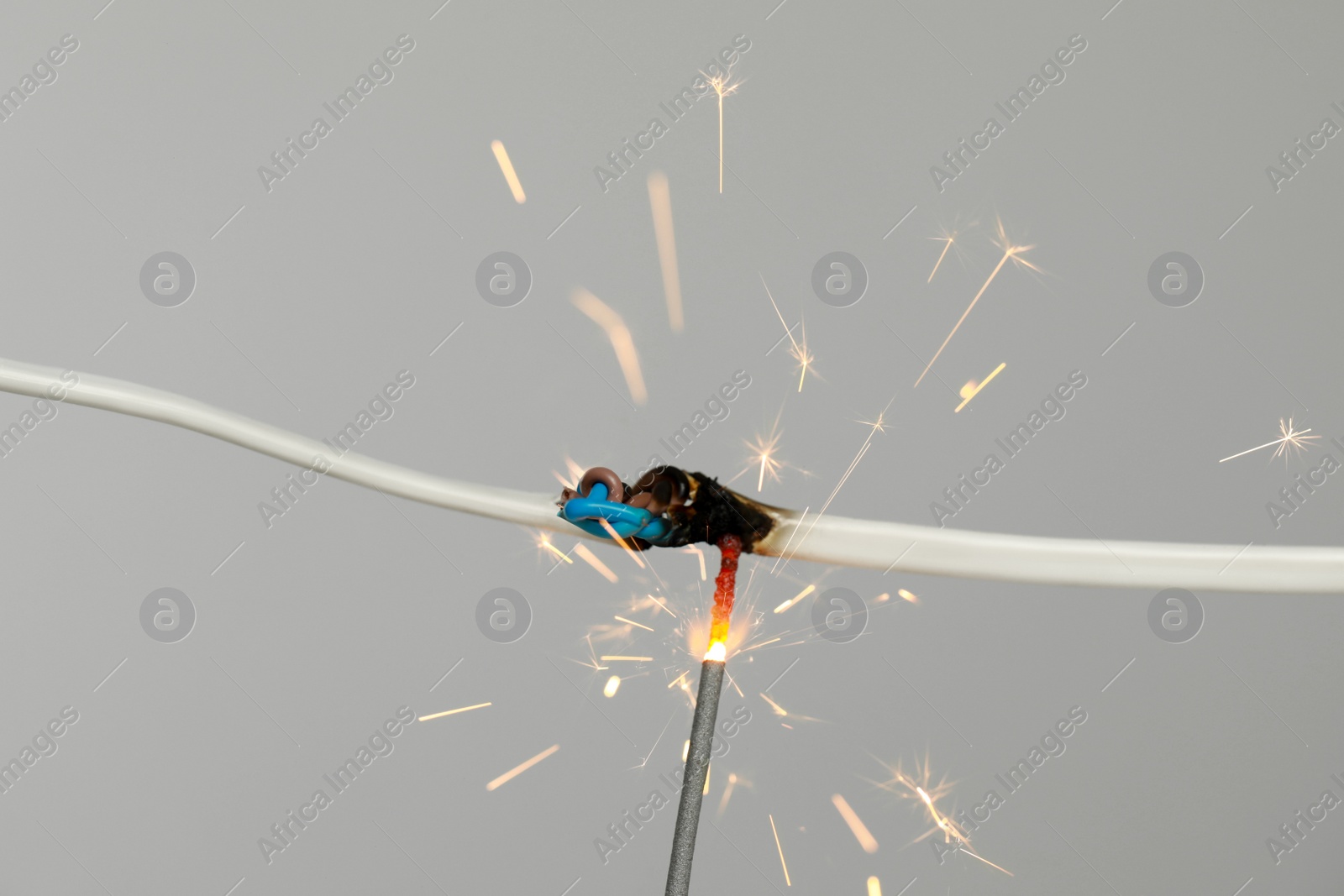 Photo of Inflamed white wire on grey background, closeup. Electrical short circuit