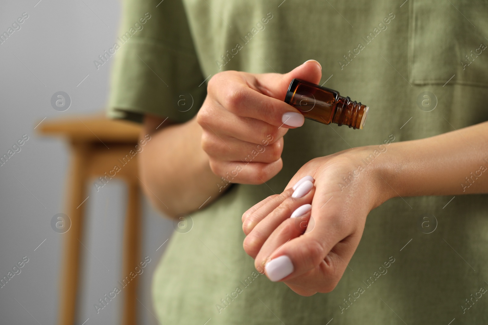 Photo of Young woman applying essential oil on wrist indoors, closeup