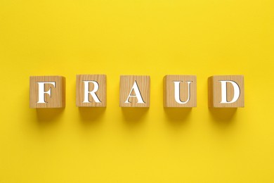 Photo of Wooden cubes with word Fraud on yellow background, flat lay