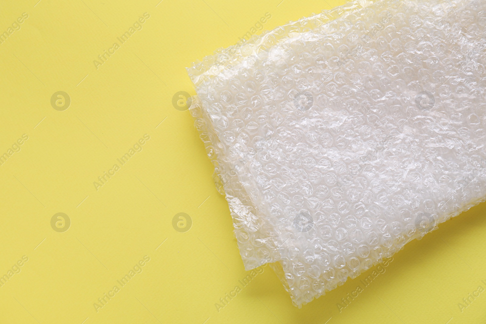 Photo of Transparent bubble wrap on yellow background, top view. Space for text