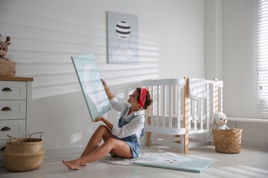 Photo of Decorator with picture on floor in baby room. Interior design