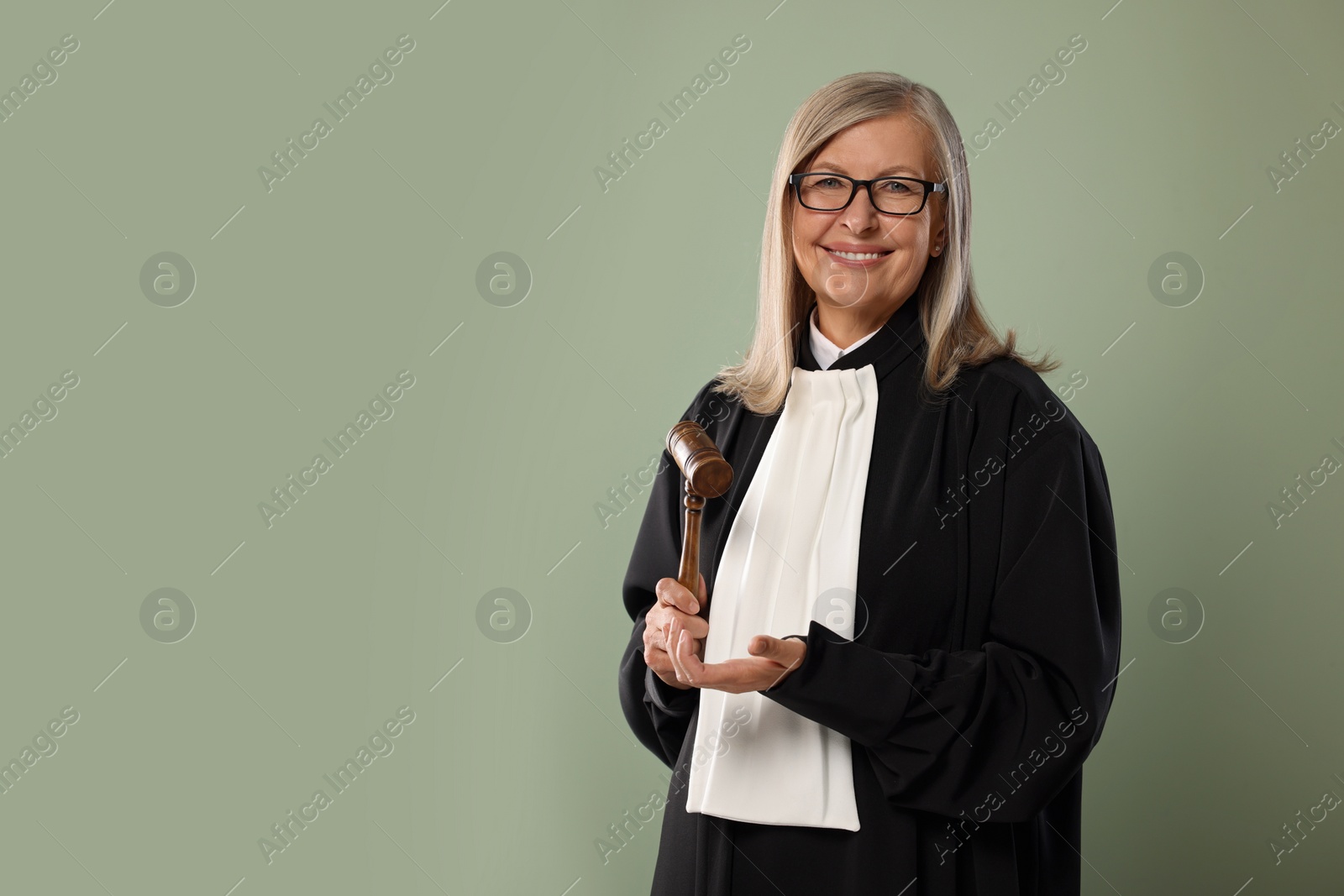 Photo of Smiling senior judge with gavel on green background. Space for text