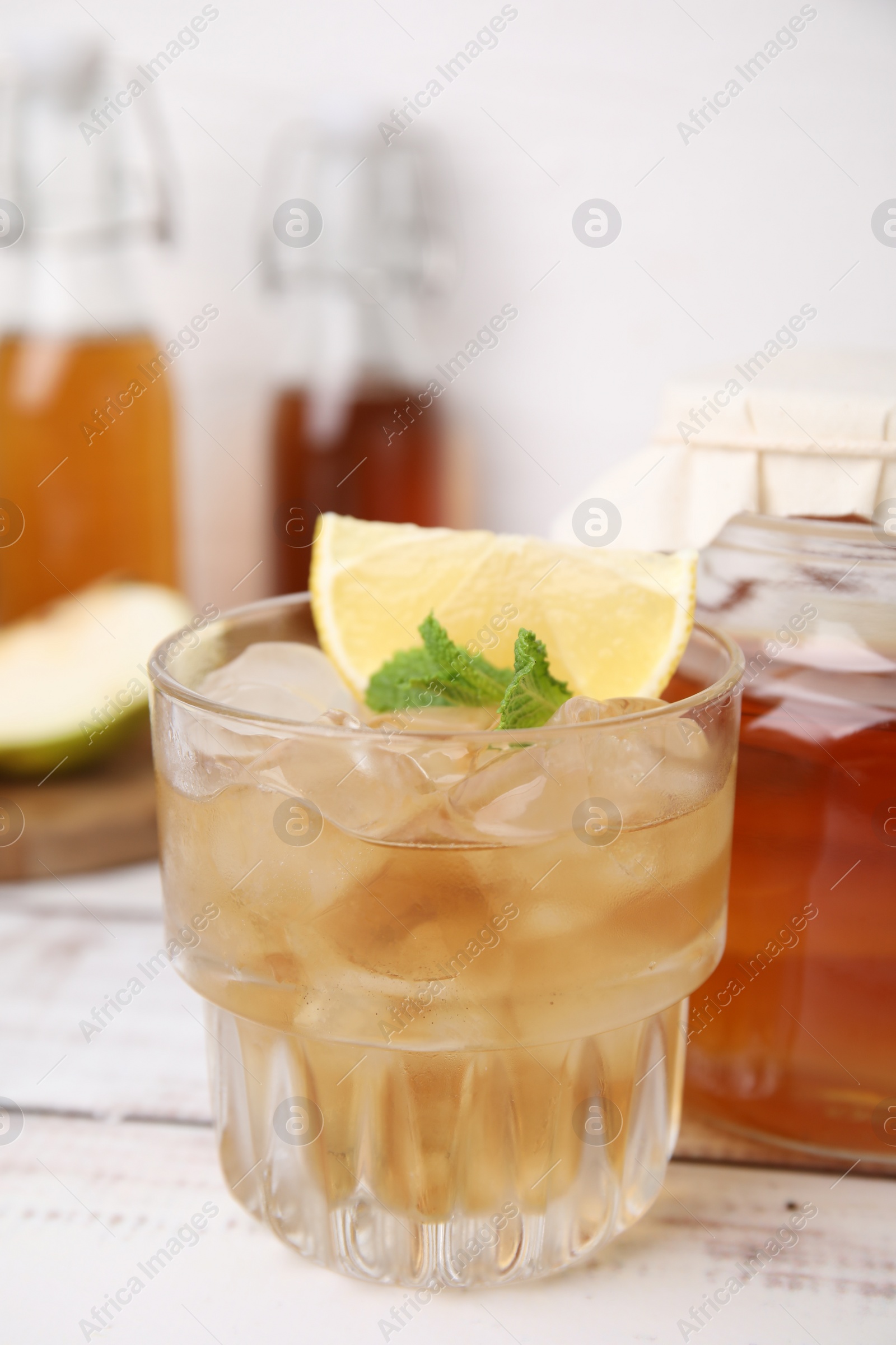 Photo of Tasty kombucha and ice cubes in glass on white wooden table, closeup