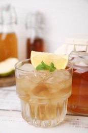 Photo of Tasty kombucha and ice cubes in glass on white wooden table, closeup