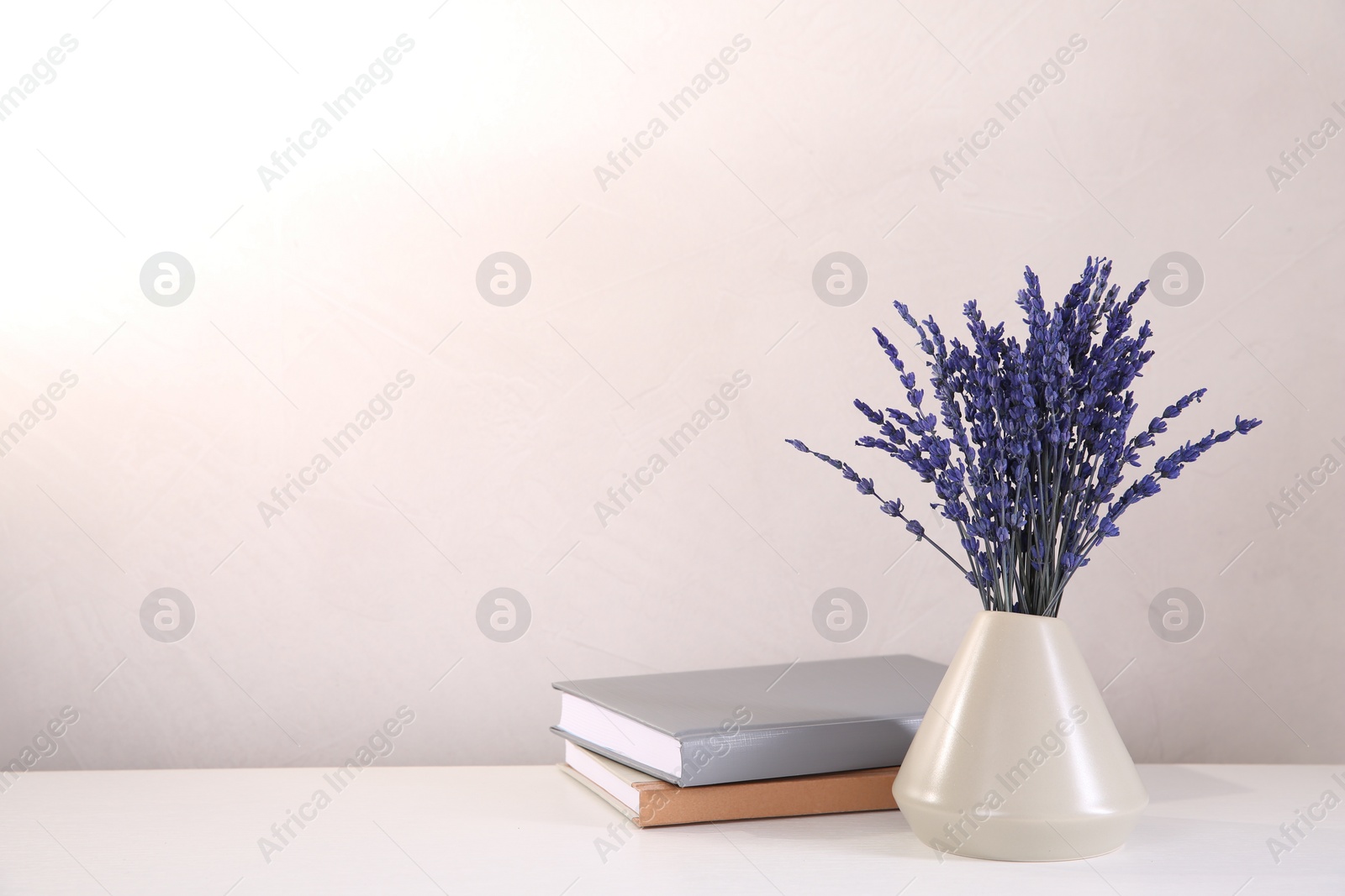 Photo of Bouquet of beautiful preserved lavender flowers and notebooks on white table near beige wall, space for text