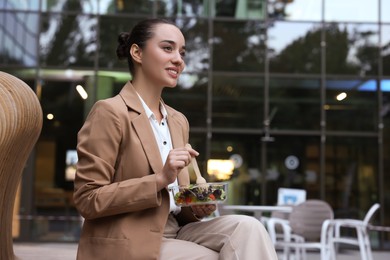 Happy young businesswoman eating lunch on bench outdoors