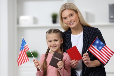 Immigration. Happy woman with her daughter holding passports and American flags indoors