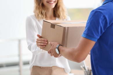 Photo of Young woman receiving parcel from courier indoors