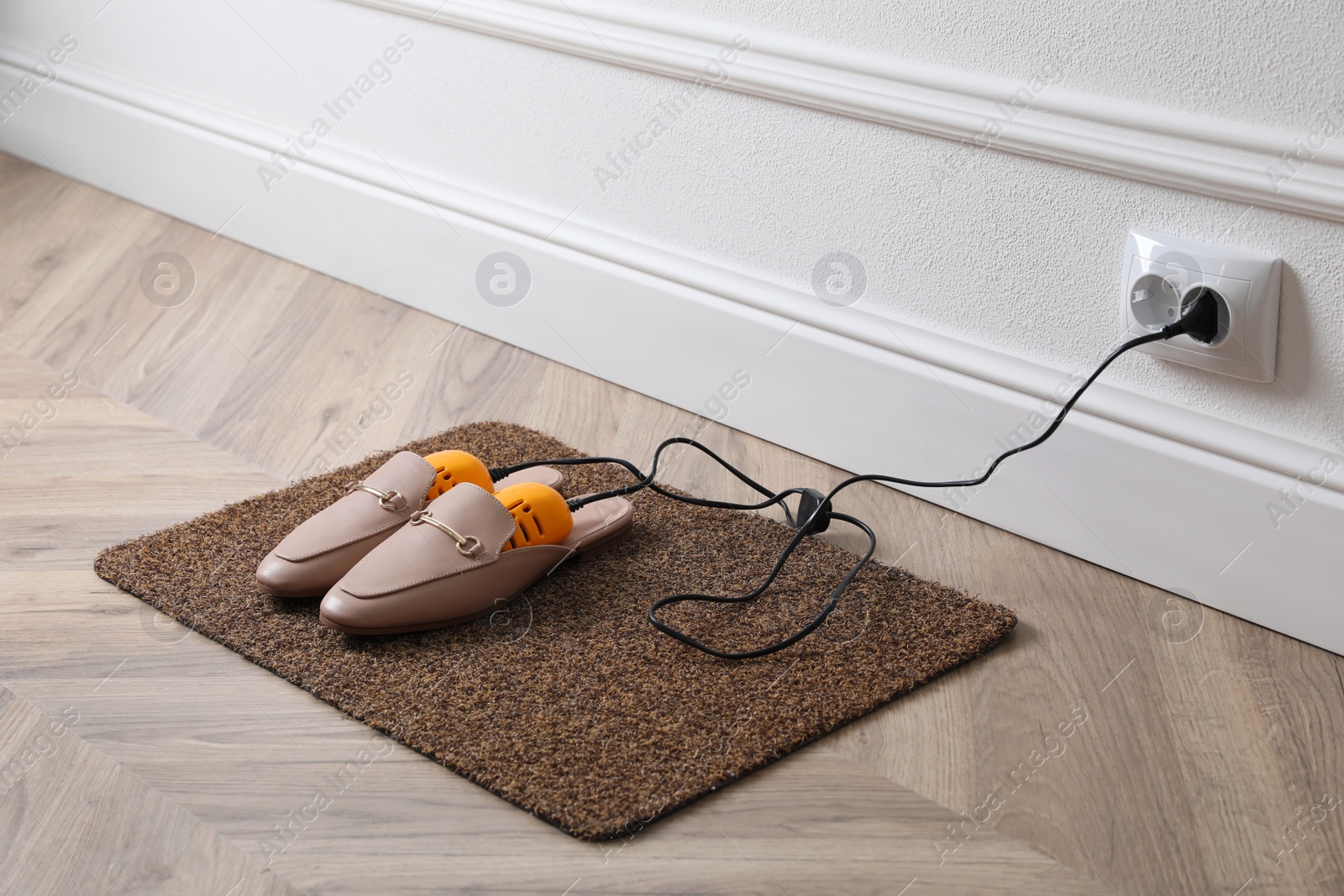 Photo of Pair of stylish shoes with modern electric footwear dryer on door mat indoors