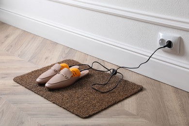 Photo of Pair of stylish shoes with modern electric footwear dryer on door mat indoors