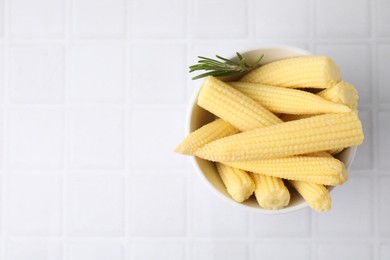 Photo of Tasty fresh yellow baby corns in bowl on white tiled table, top view. Space for text