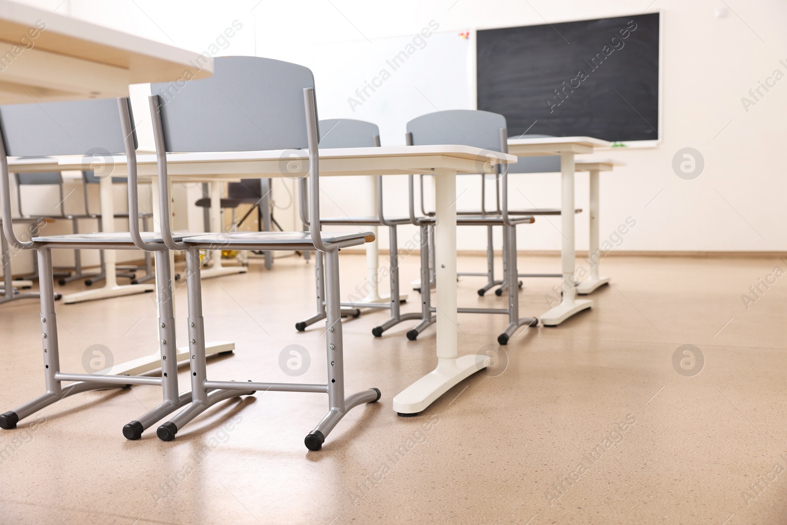 Photo of Empty school classroom with desks, blackboard and chairs