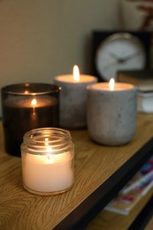 Photo of Lit candles in different holders on wooden table indoors. Space for text