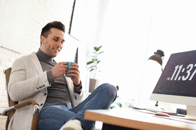 Photo of Young man with cup of drink relaxing at table in office during break