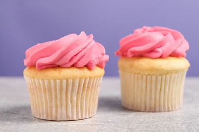 Photo of Delicious cupcakes with bright cream on gray table against violet background