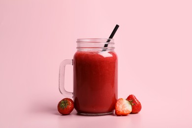Photo of Mason jar with delicious berry smoothie and fresh strawberries on pink background