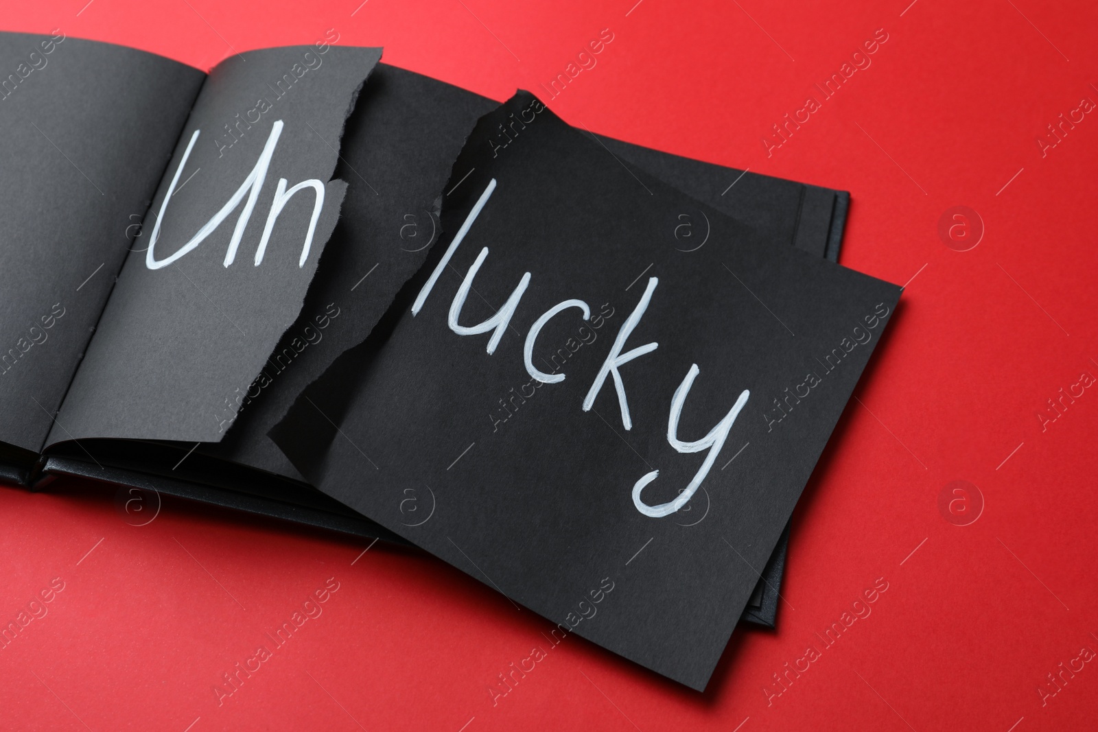 Photo of Torn word UNLUCKY written in notebook on red background