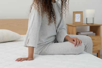 Photo of African American woman sitting on soft mattress in bedroom, closeup