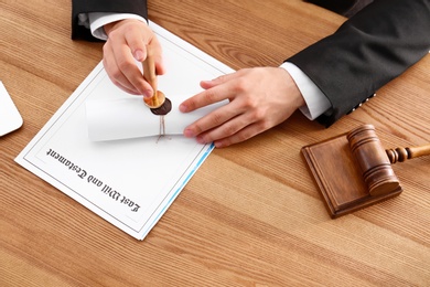 Photo of Male notary sealing document at wooden table, closeup
