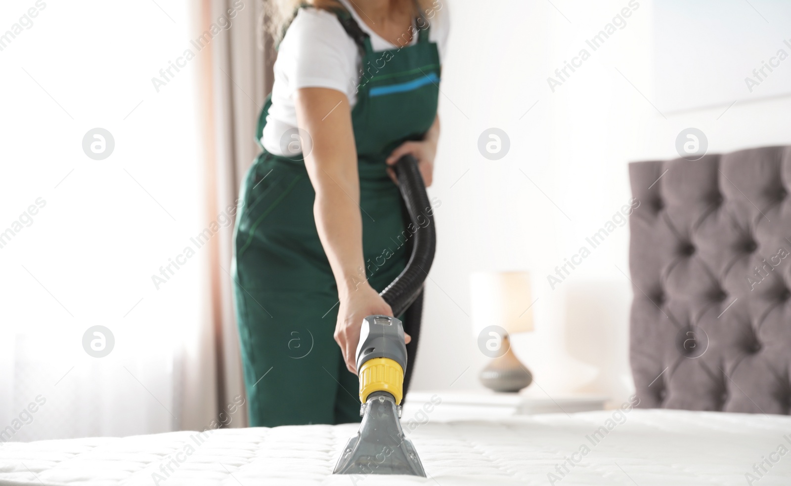 Photo of Janitor cleaning mattress with professional equipment in bedroom, closeup
