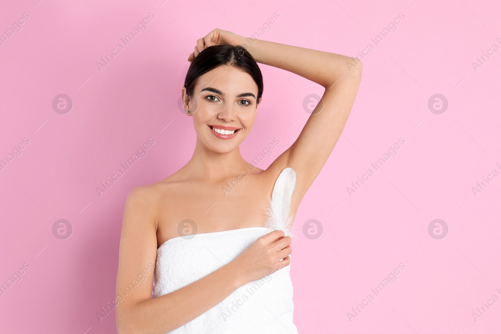 Photo of Young woman touching armpit with feather after epilation procedure on pink background