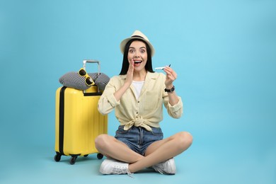 Photo of Happy female tourist with toy plane, suitcase and travel pillow on light blue background